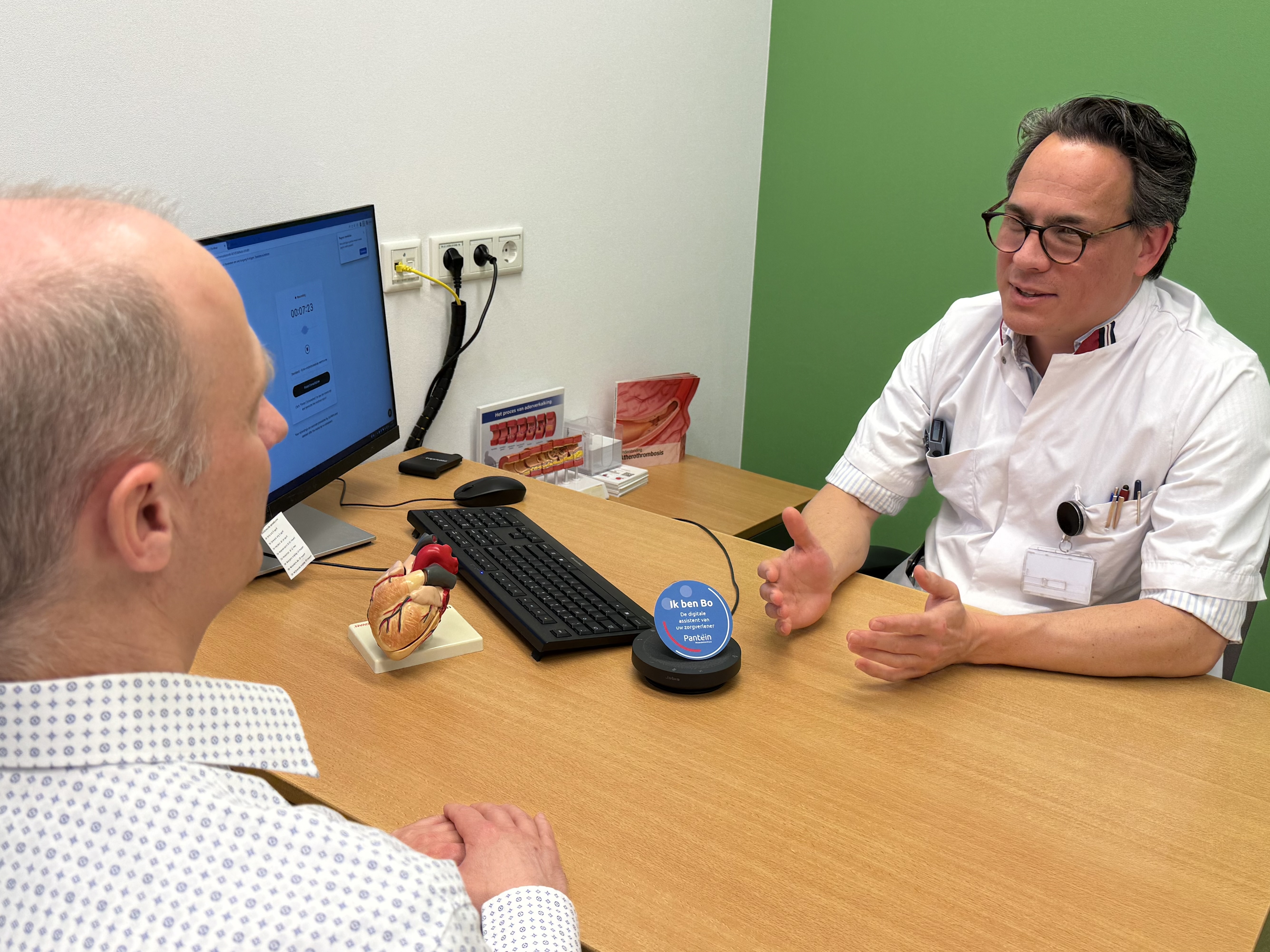 Cardioloog Bart Driesen in gesprek met patiënt, digitale assistent Bo luistert mee Cardioloog Bart Driesen in gesprek met patiënt, digitale assistent Bo luistert mee